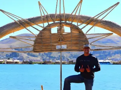 Rob Tatum posing by a large wooden sun sculpture over turquoise water with mountains in the background.