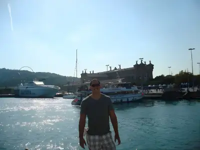 Rob Tatum standing by a sunny harbor with boats and waterfront buildings in the background.