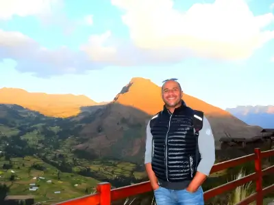 Rob Tatum smiling at a mountain overlook during sunset, standing by a red railing with green valleys and peaks in the background.