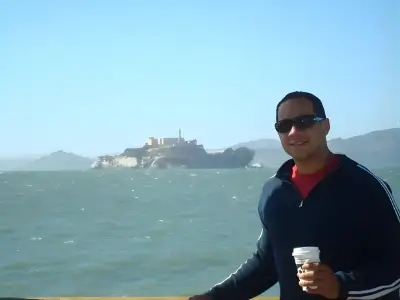 Rob Tatum standing by the waterfront holding a coffee, with Alcatraz Island visible in the background on a sunny day.