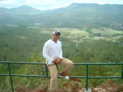 Rob Tatum sitting on a railing overlook with a mountain valley landscape in the background.