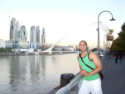 Rob Tatum posing along a waterfront promenade with a city skyline and modern bridge in the background.