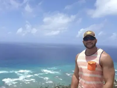 Rob Tatum smiling at a coastal overlook with turquoise ocean waves and a bright blue sky in the background.