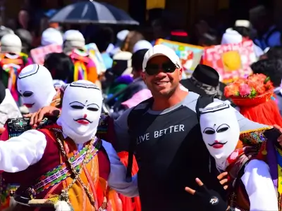 Rob Tatum smiling with performers in colorful traditional costumes and white masks at a lively outdoor festival.