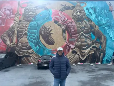 Rob Tatum standing in front of a large, colorful mural featuring two muscular fantasy figures in a city parking area.