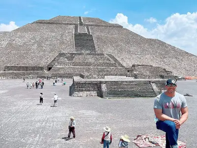 Rob Tatum posing in front of the Pyramid of the Sun at Teotihuacan on a bright day with visitors in the background.