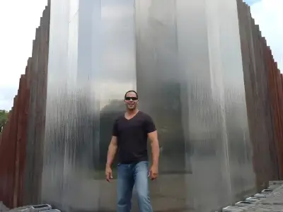 Rob Tatum standing in front of a tall modern water feature with cascading water walls, wearing sunglasses, a black shirt, and jeans.