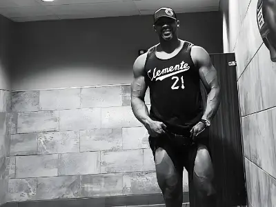 Rob Tatum posing in a gym locker room wearing a basketball jersey, showing muscular legs in a black-and-white photo.
