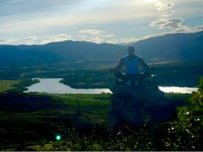 Rob Tatum sitting on a rock overlook above a lake and valley at sunset, surrounded by mountains.