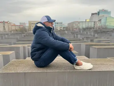 Rob Tatum sitting on a concrete structure at an outdoor memorial site, with a cityscape in the background.