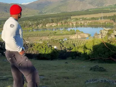 Rob Tatum overlooking a scenic valley and lake from a hillside, wearing a red beanie and casual outdoor clothing.