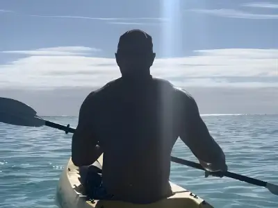Rob Tatum kayaking on calm ocean water, silhouetted against a bright sky and sunlight.