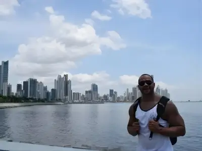 Rob Tatum smiling by the waterfront with a modern city skyline and cloudy blue sky in the background.