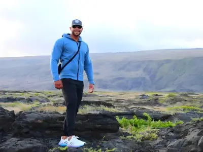 Rob Tatum standing on rocky terrain in a blue jacket and cap, with rolling hills in the background.