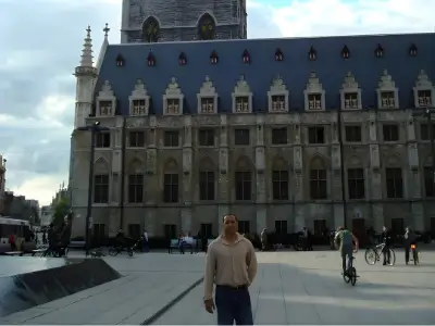 Rob Tatum standing in a large public square in front of an ornate historic building, wearing a beige sweater and jeans.