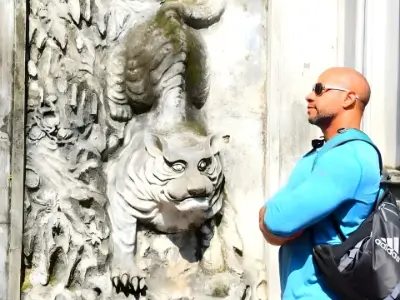 Rob Tatum wearing sunglasses and a blue shirt, standing beside a carved tiger sculpture with a backpack over one shoulder.