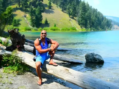 Rob Tatum sitting on a log by a turquoise lake, with forested hills in the background.